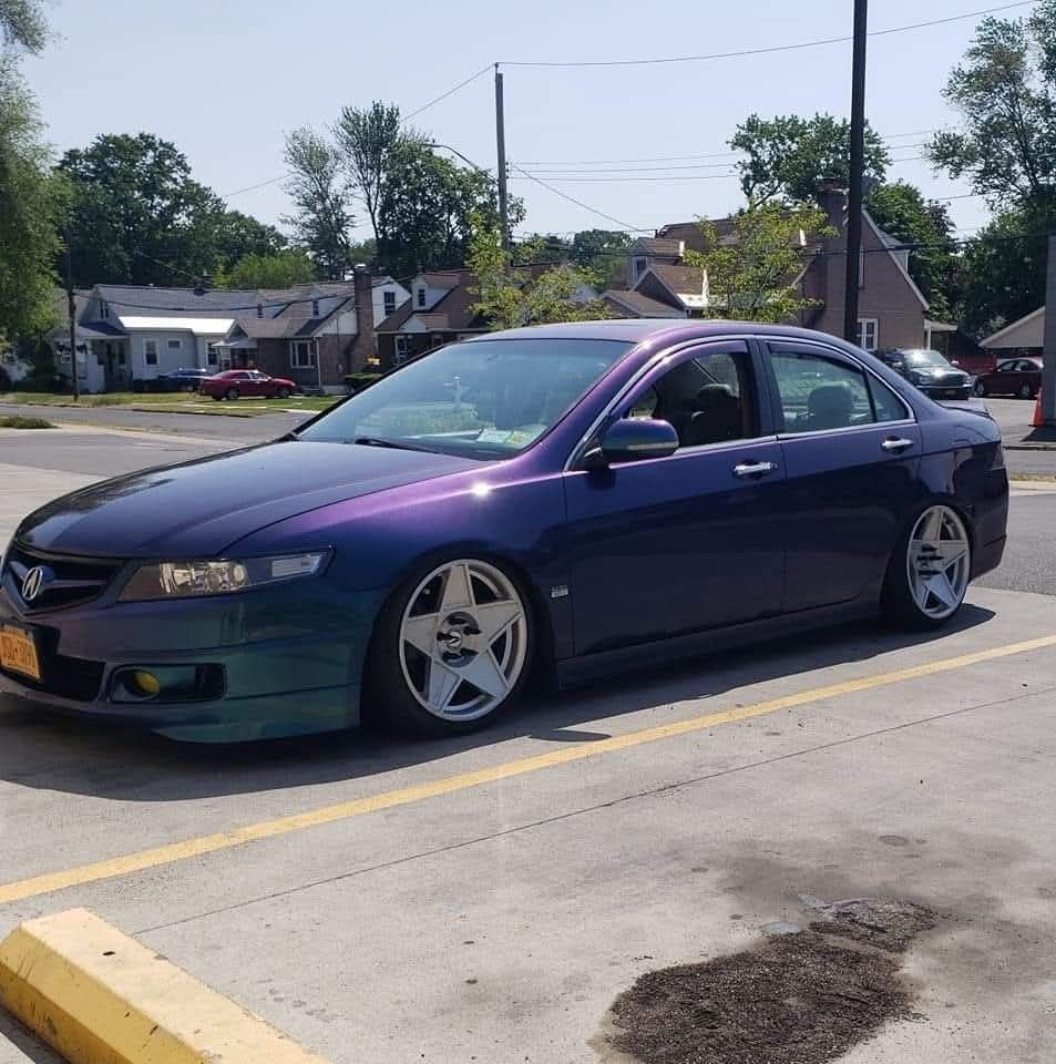 Blue-purple customized car with silver wheels parked on the side of the road, sunny day.