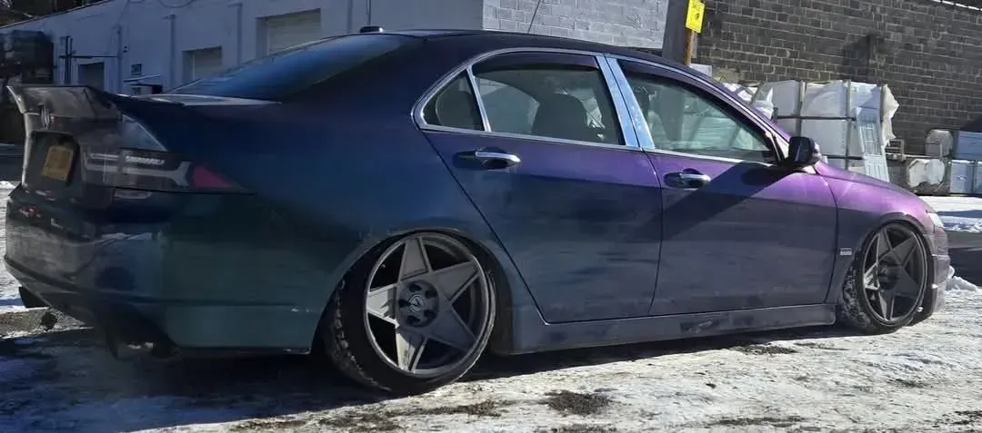 A lowered, custom purple car with unique wheels parked on snow. A large spoiler is on the trunk.
