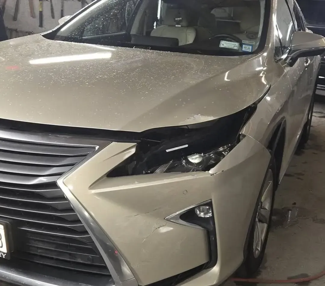 Beige Lexus RX with front damage, likely in a repair shop.