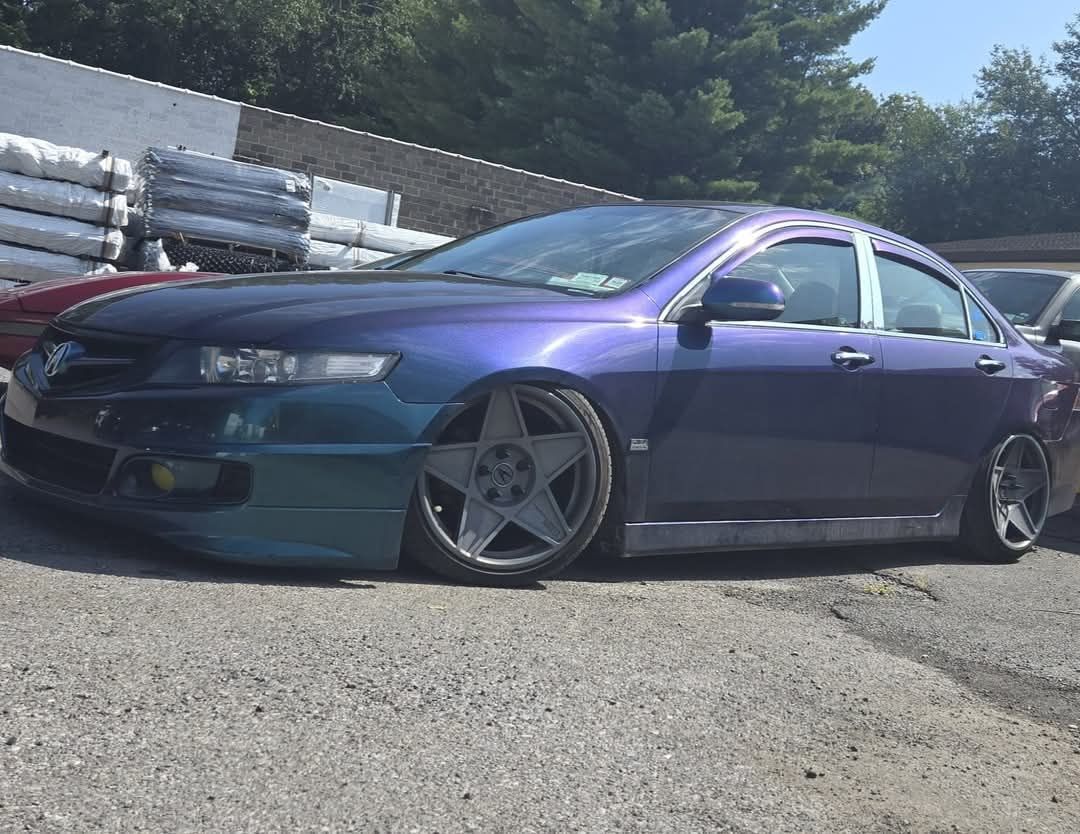 Blue and teal lowered car with five-spoke wheels parked on gravel, sunny outdoor setting.