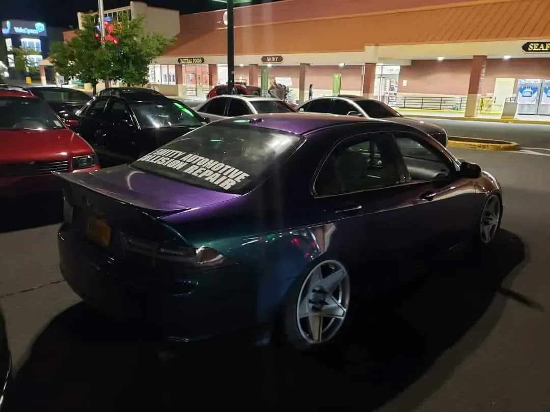Purple-green iridescent car in a parking lot.  Has lowered suspension and custom wheels.