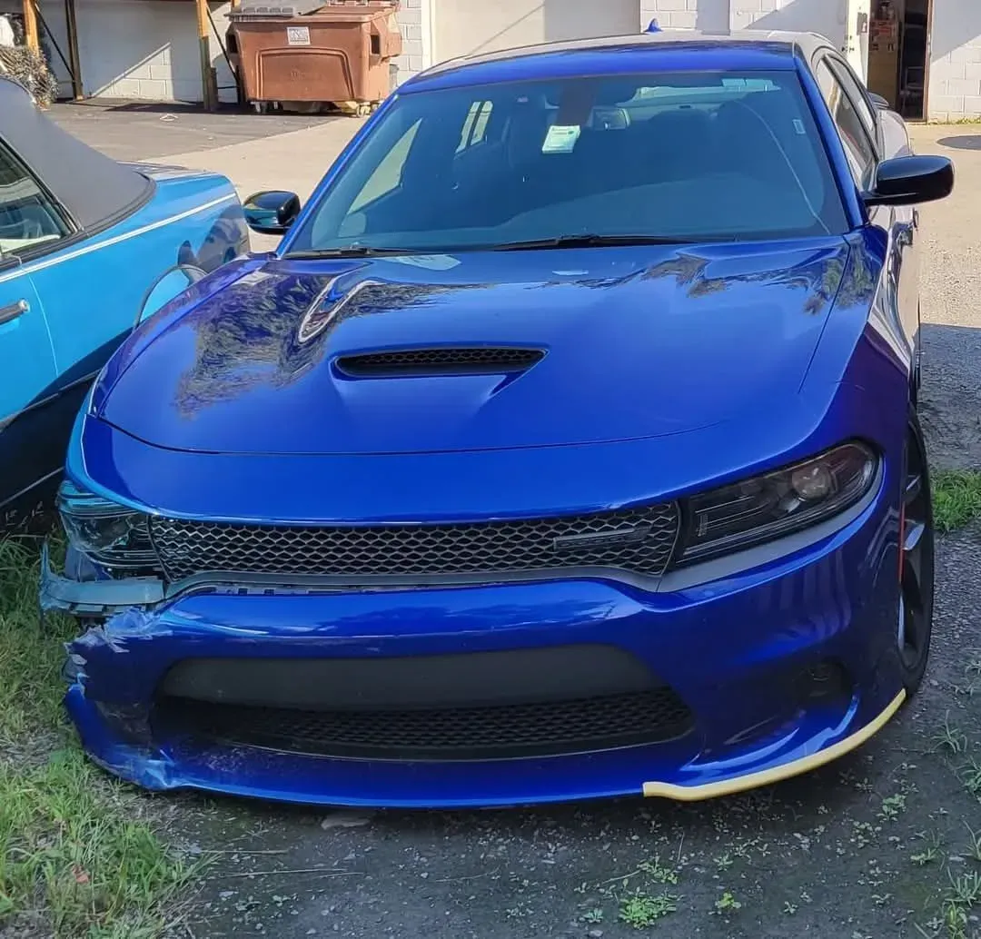 Blue Dodge Charger with front-end damage, parked outside, on grass.