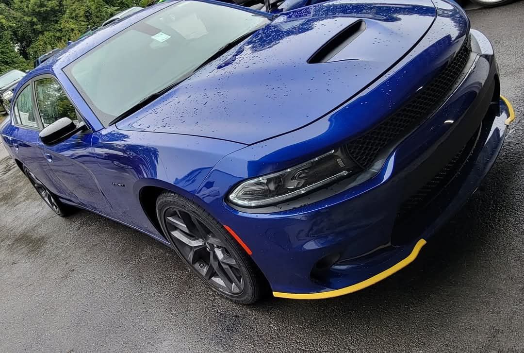 Blue Dodge Charger with yellow trim, parked on a wet pavement.