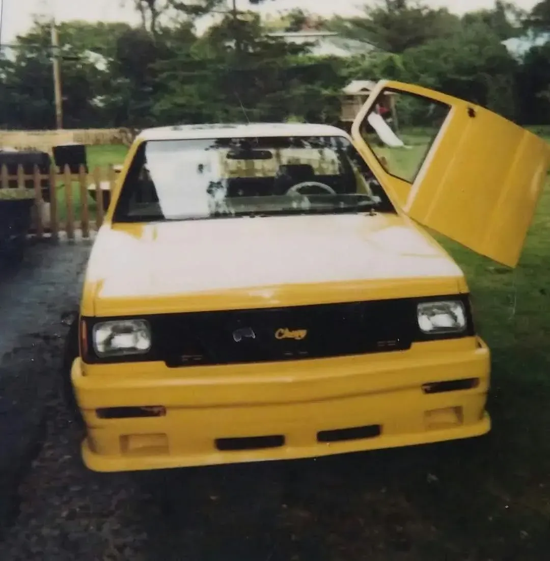 Yellow customized Chevy with gull-wing door open, parked on a driveway.
