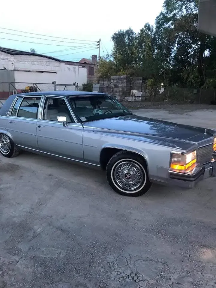 Silver Cadillac sedan parked outside, chrome accents, white-wall tires, dusk setting.