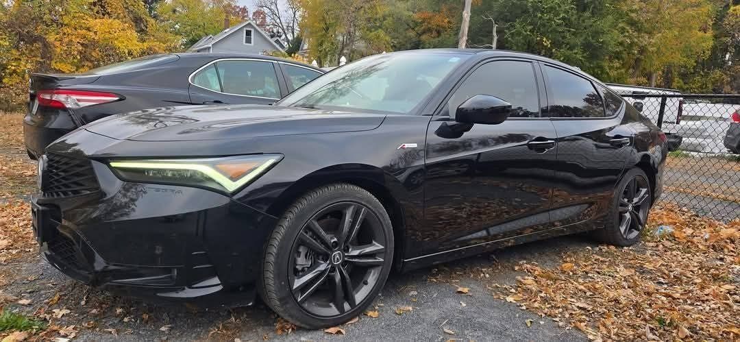 Black Acura sedan parked on asphalt with fallen leaves; another car behind it.