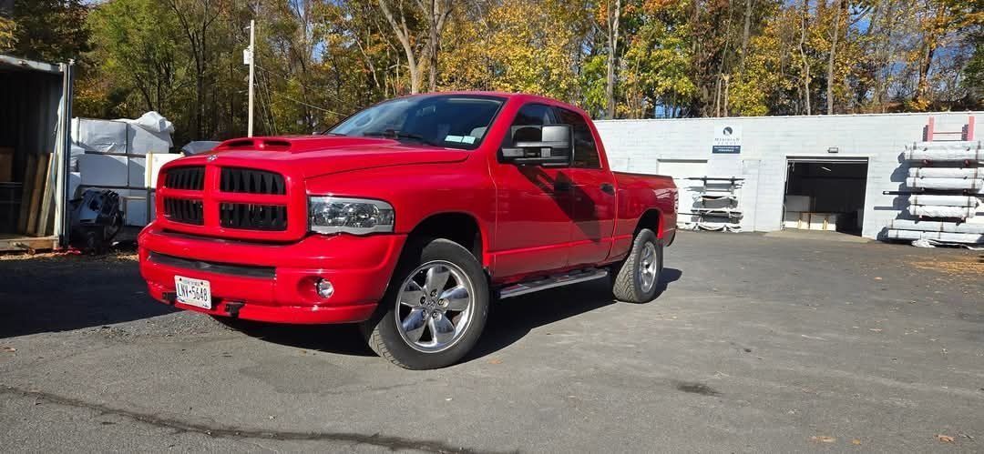 Red Dodge Ram pickup truck parked in front of a building with the woods in the background.