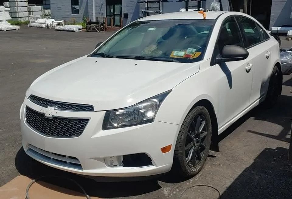 White Chevrolet Cruze sedan parked outdoors, dark wheels, sunny day.