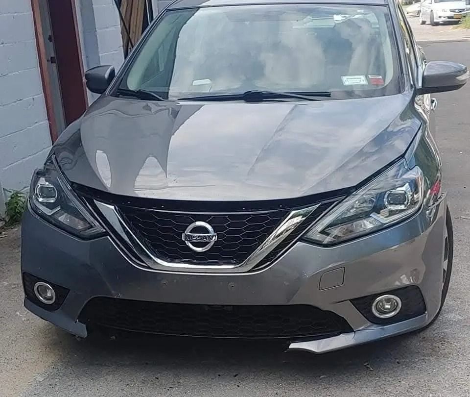 Gray Nissan Sentra parked in front of a building; dark gray grill, headlights, and fog lights.