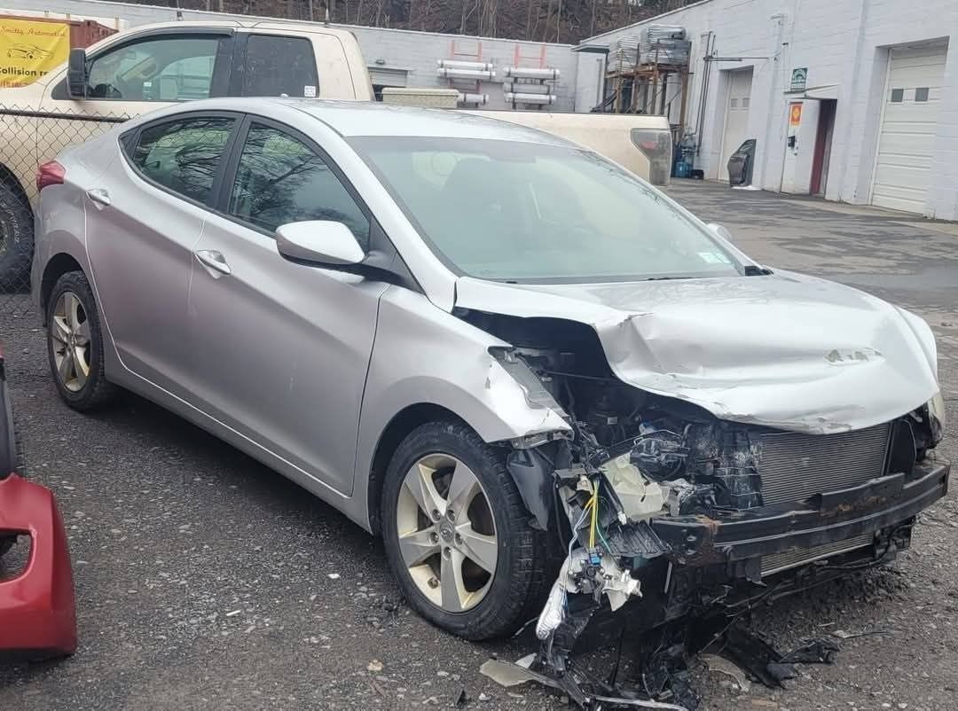 Silver Hyundai Elantra damaged in a collision, front end heavily impacted, in a yard.