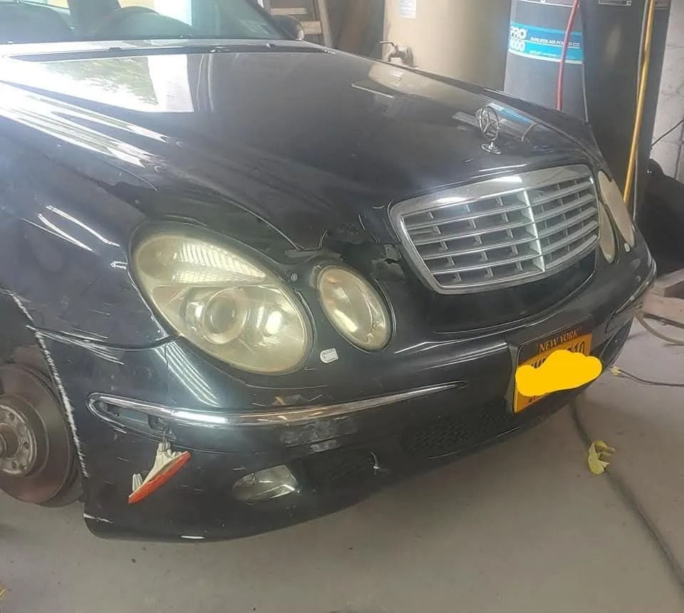 Dark blue Mercedes-Benz car with front-end damage, in a repair shop.