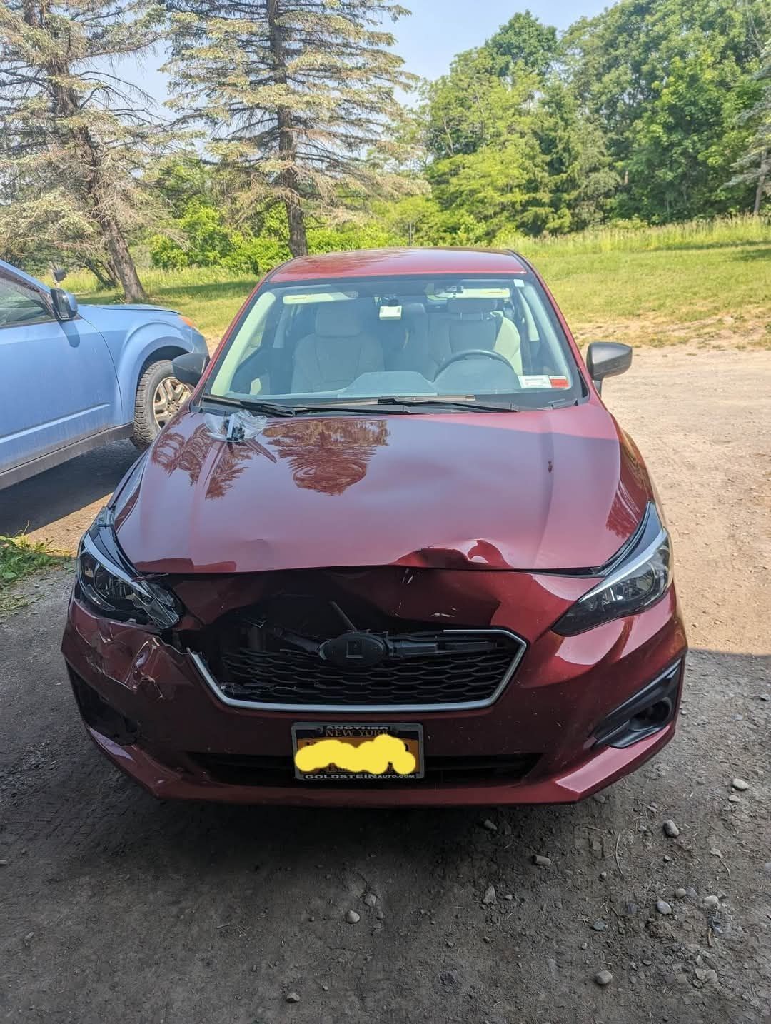 Red Subaru Impreza with front-end damage, parked outdoors on a sunny day.