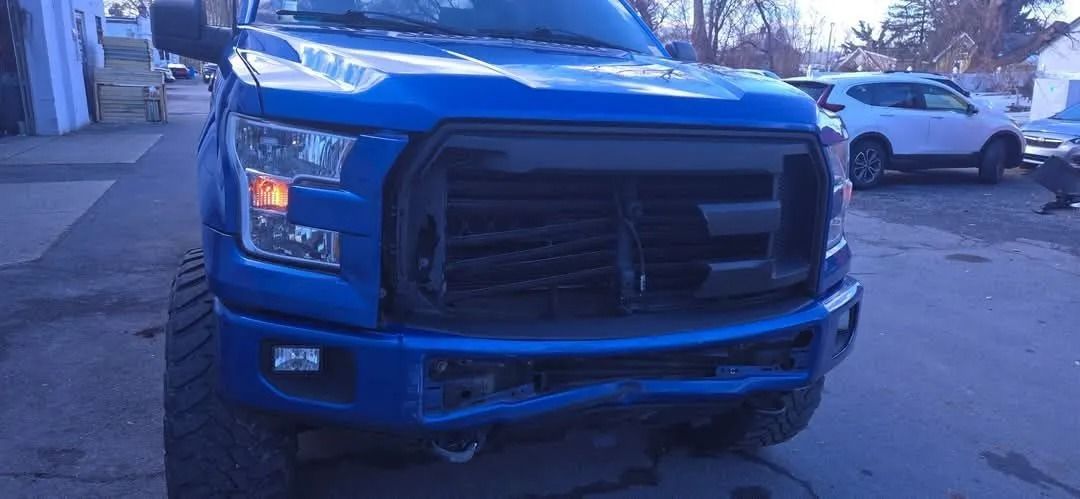 Blue Ford truck with black grille and damaged bumper.