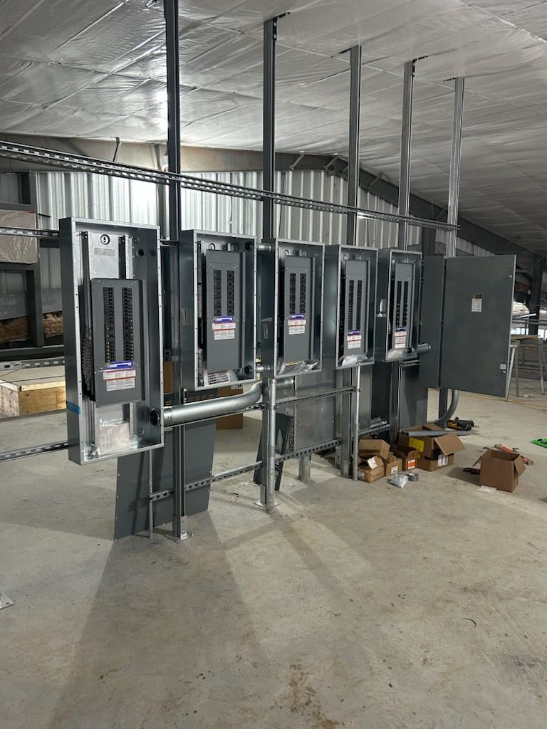 Row of electrical circuit breaker panels in an unfinished basement with exposed wiring and concrete floor