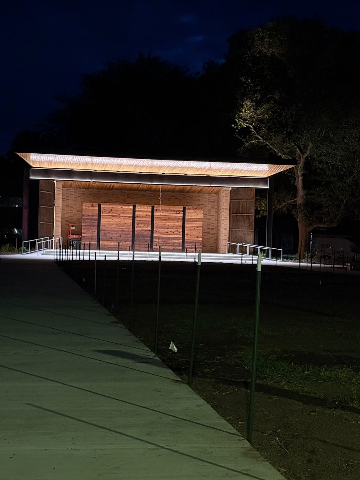 Night view of a small lit brick building with a white roof overhang and green foreground netting.