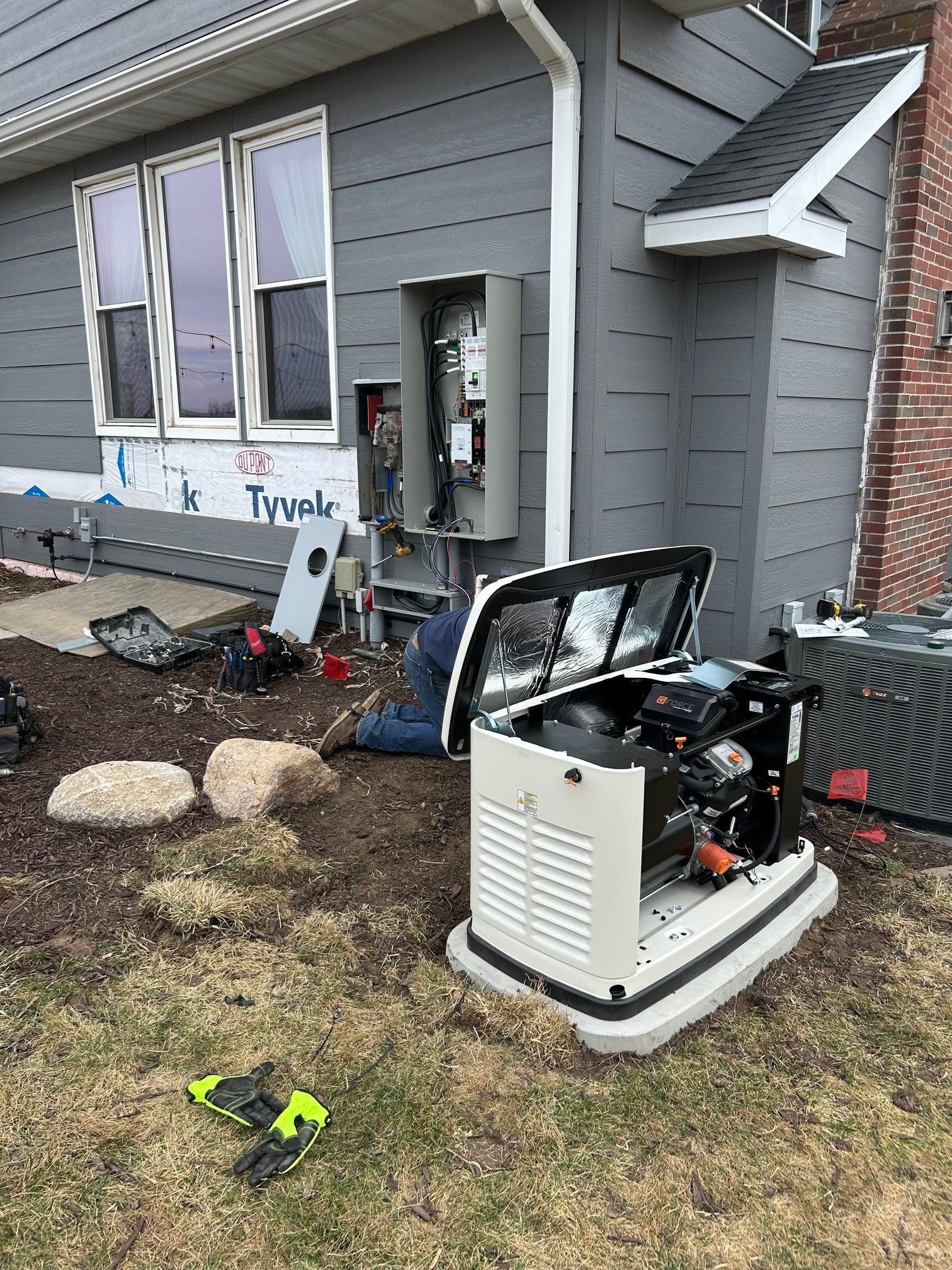 A man is working on a generator in front of a house.
