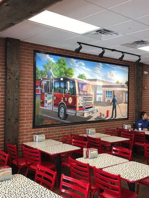 A restaurant with tables and chairs and a large painting of a fire truck on the wall