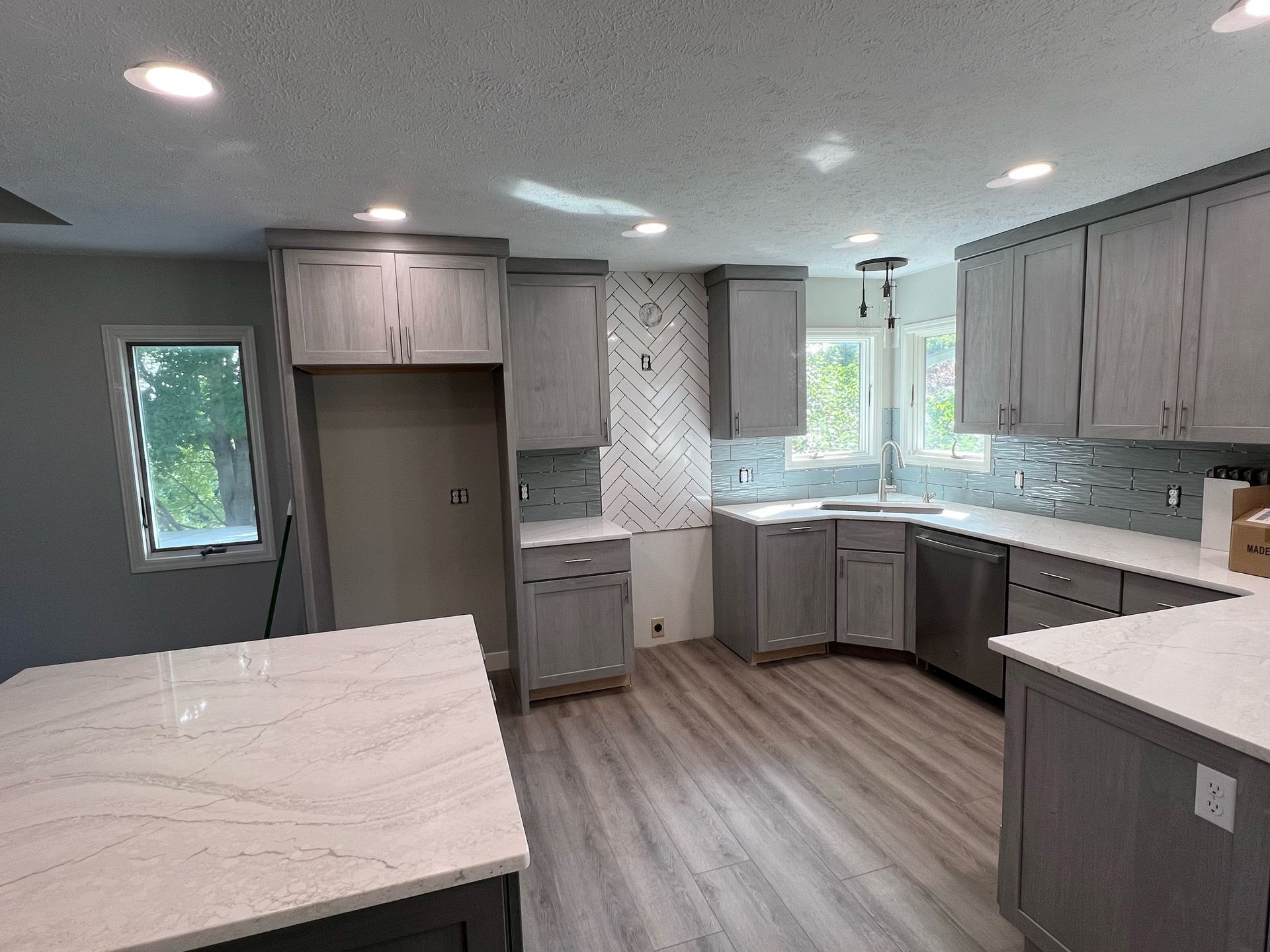 A kitchen with gray cabinets and white counter tops.