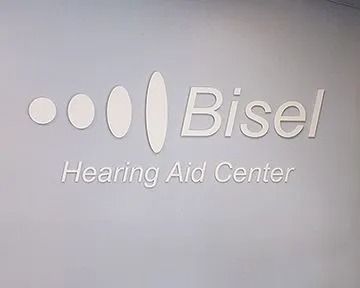 Logo for Bisel Hearing Aid Center: white text and design on a gray wall.