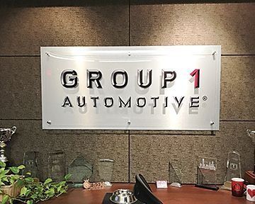 Group 1 Automotive logo on a metal plaque, mounted on a textured wall.