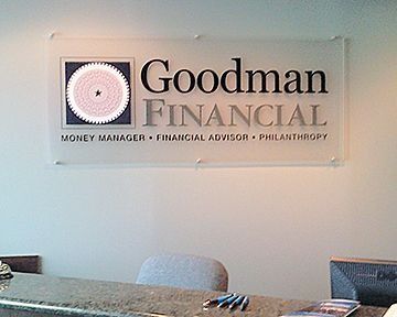 Goodman Financial sign on a wall above a desk. Gray and black text with logo of a starburst.
