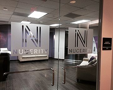 Glass door entrance to Nucerity office with logo and seating area visible.