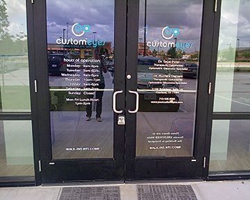 Glass double doors of Custom Eyes eye clinic with operating hours and doctor information.