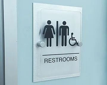 Restroom sign with female, male, and wheelchair symbols on a light blue wall. 