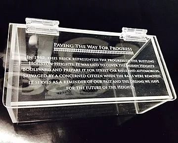 Clear acrylic box with engraved text about a brick from 1912, commemorating progress in Hollion Heights.
