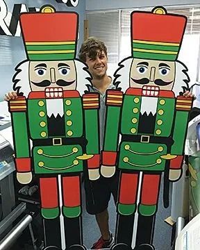 Man smiling, holding two large green, red, and black nutcracker cutouts.