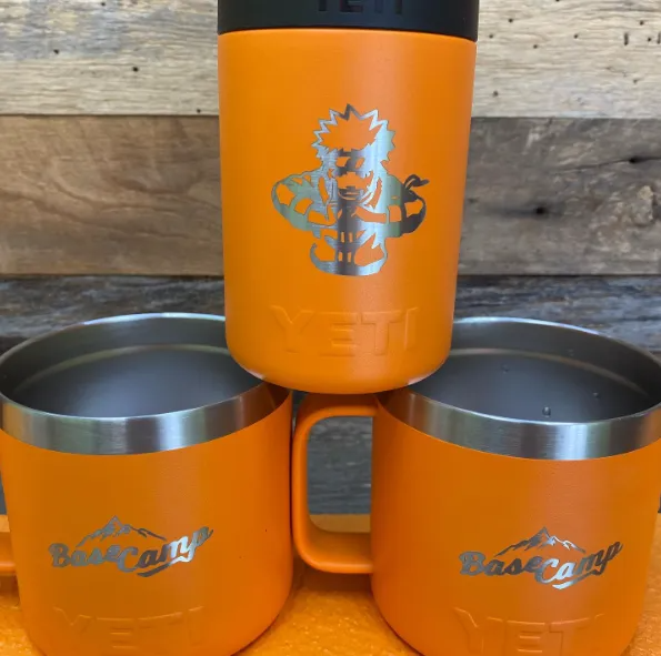 Three orange Yeti mugs with silver logos. One is a can cooler, the other two have handles.