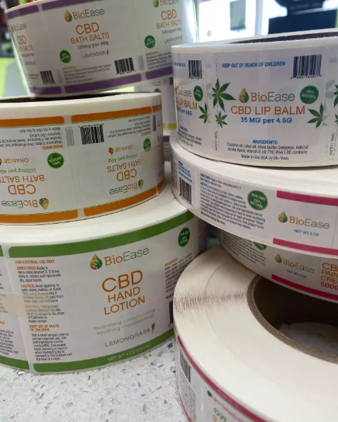 Rolls of CBD product labels, including hand lotion, bath balm, and lip balm. White and green branding.