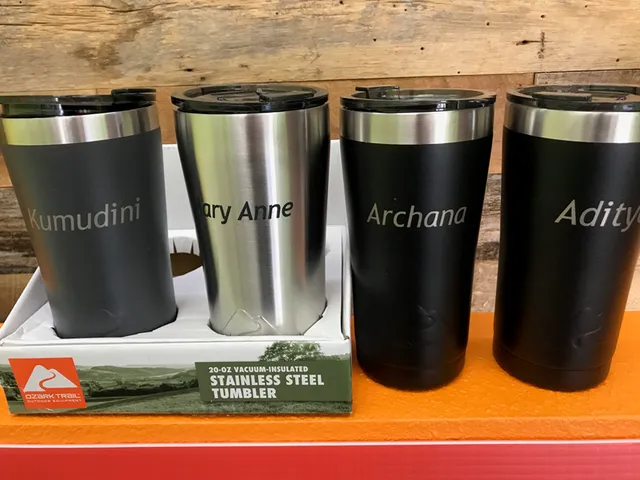Four engraved stainless steel tumblers with names. Dark and silver colors with black lids, in a box.