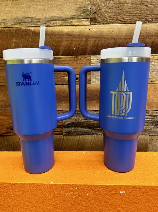 Two blue Stanley travel mugs with handles and straws; one has Stanley logo, other has text and image.
