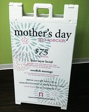 White sandwich board sign with Mother's Day Spa Specials. Text includes pricing, treatments, and florist information.