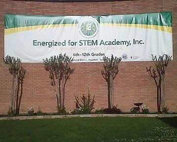 Banner for Energized for STEM Academy, Inc. on a brick wall with small trees and bushes in front.