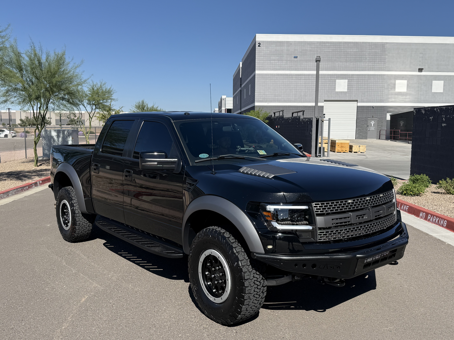 A black lifted pickup truck parked outdoors beside a modern building under a clear blue sky