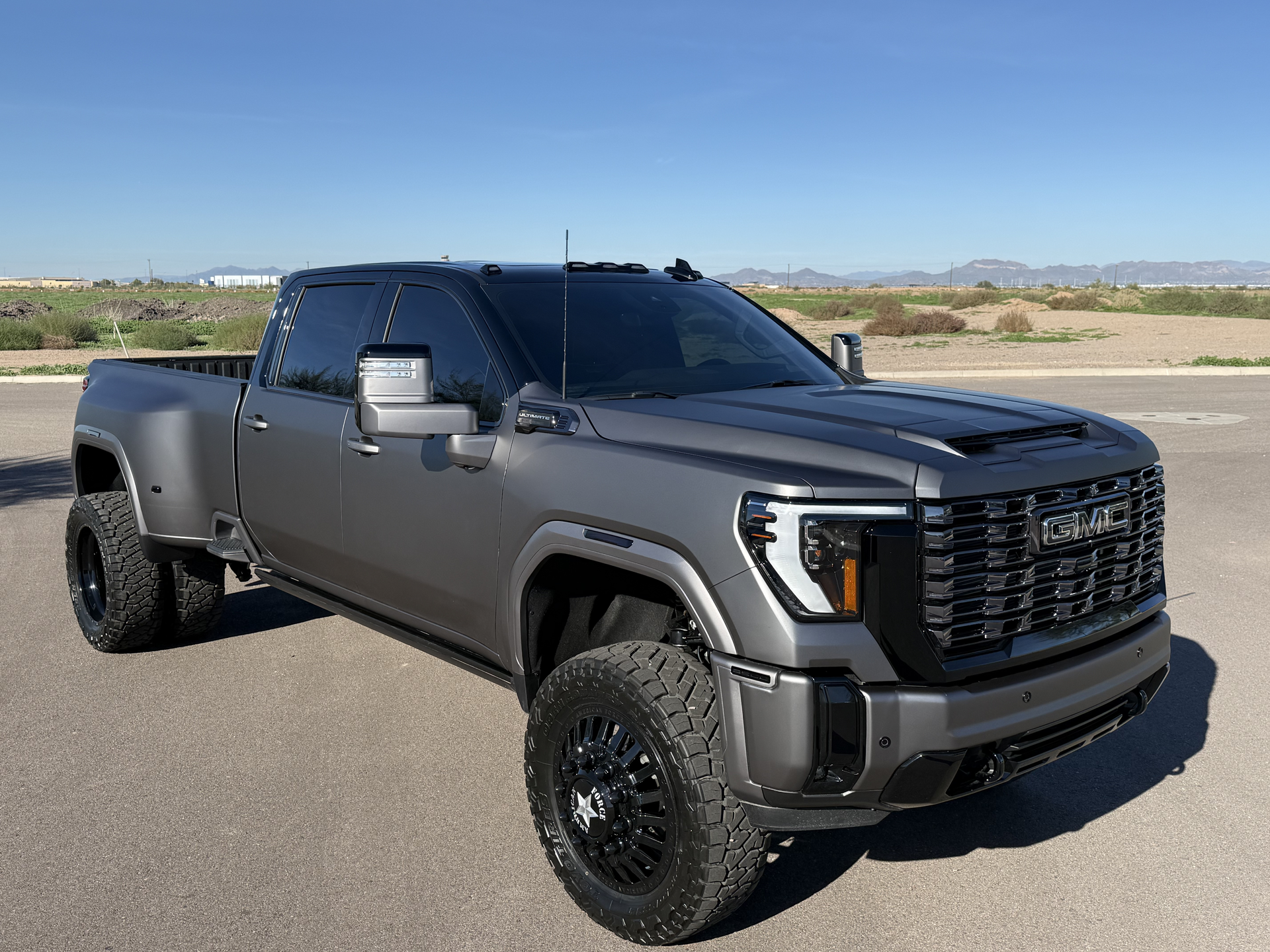 Dark gray lifted pickup truck parked on a road in a desert landscape