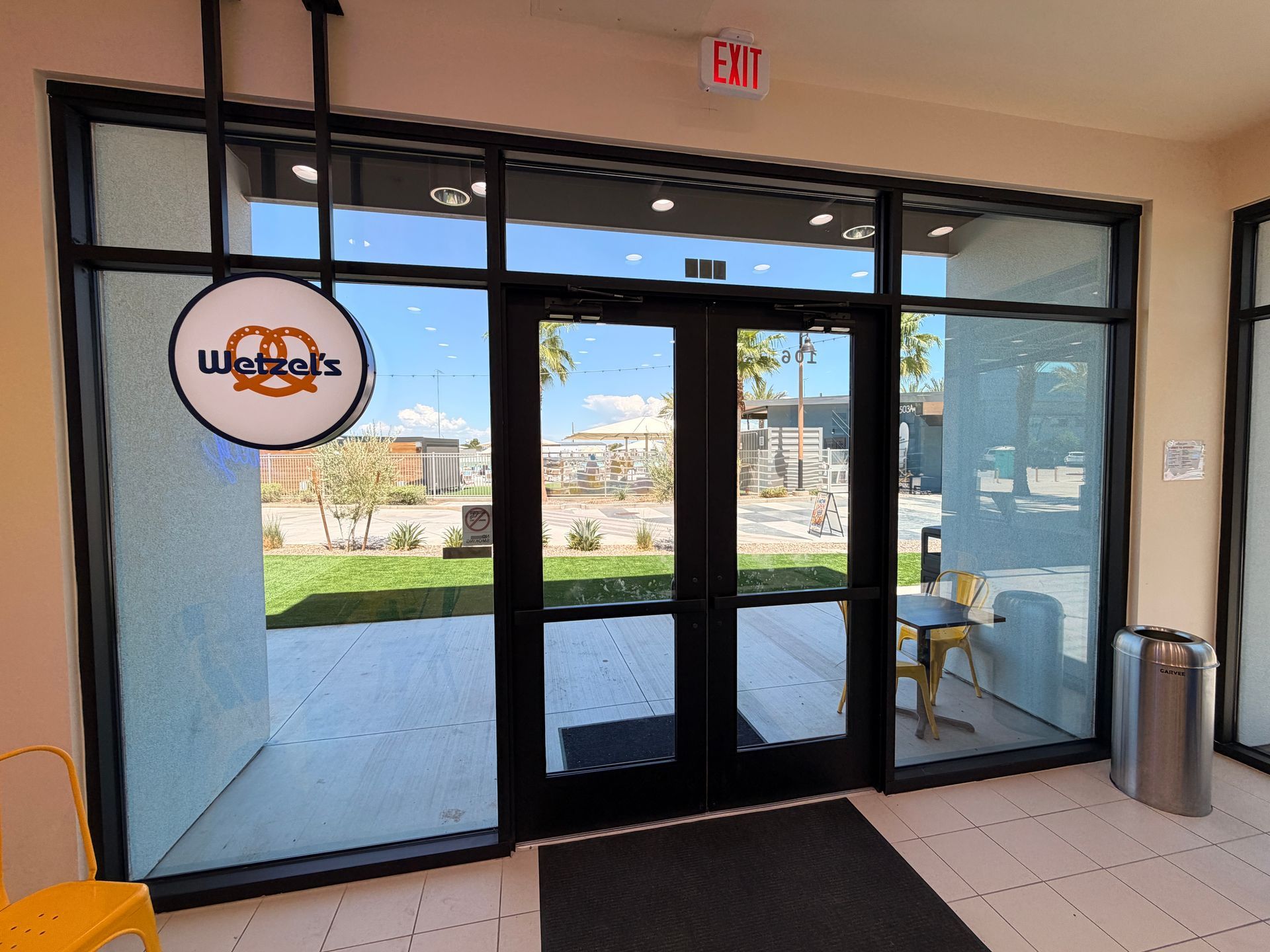 Glass storefront entrance with sliding doors, exit sign, and outdoor view beyond.
