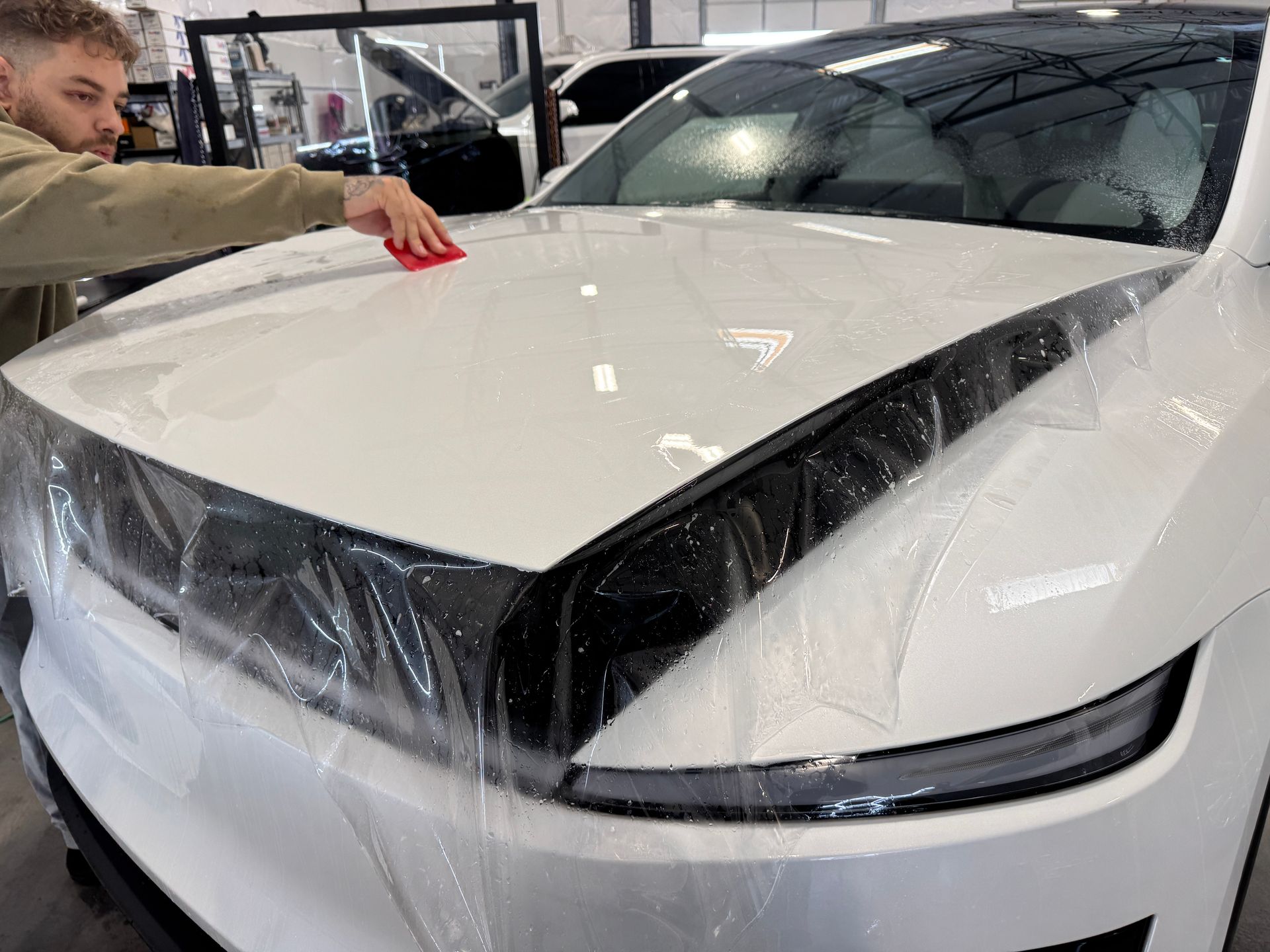 Person smoothing protective film on the front of a white car in a garage