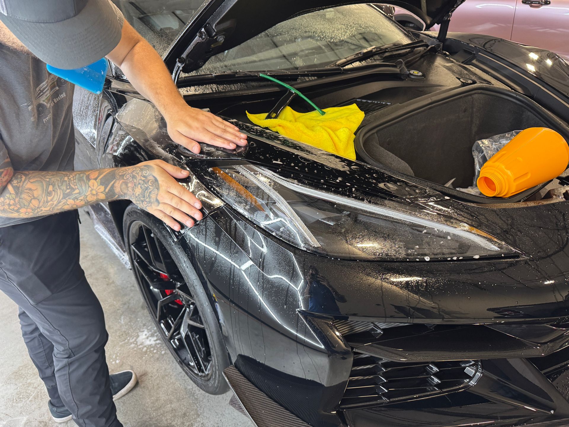 Person washing a black sports car with soap and sponge in a driveway