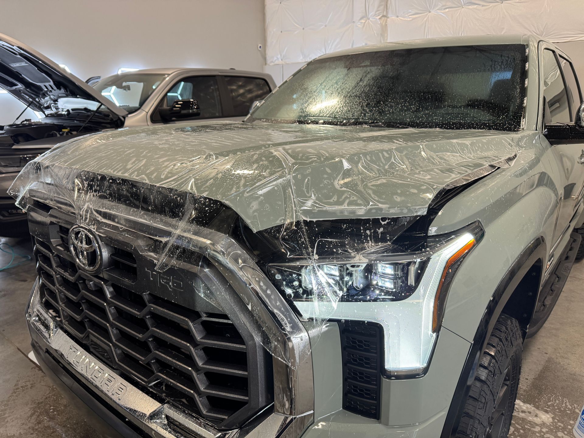 White pickup truck covered in soap suds inside a car wash bay