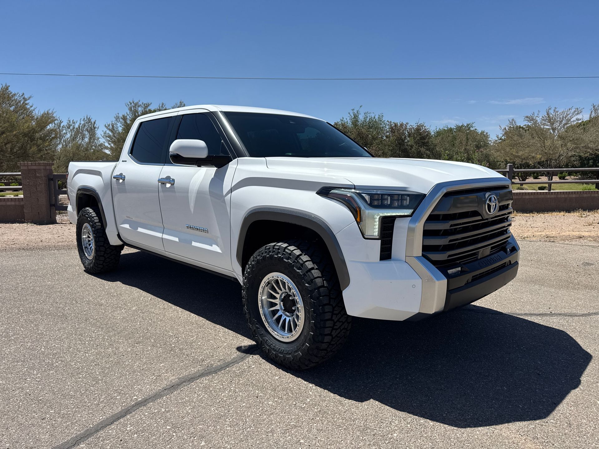 White lifted pickup truck parked on a paved road under a clear blue sky