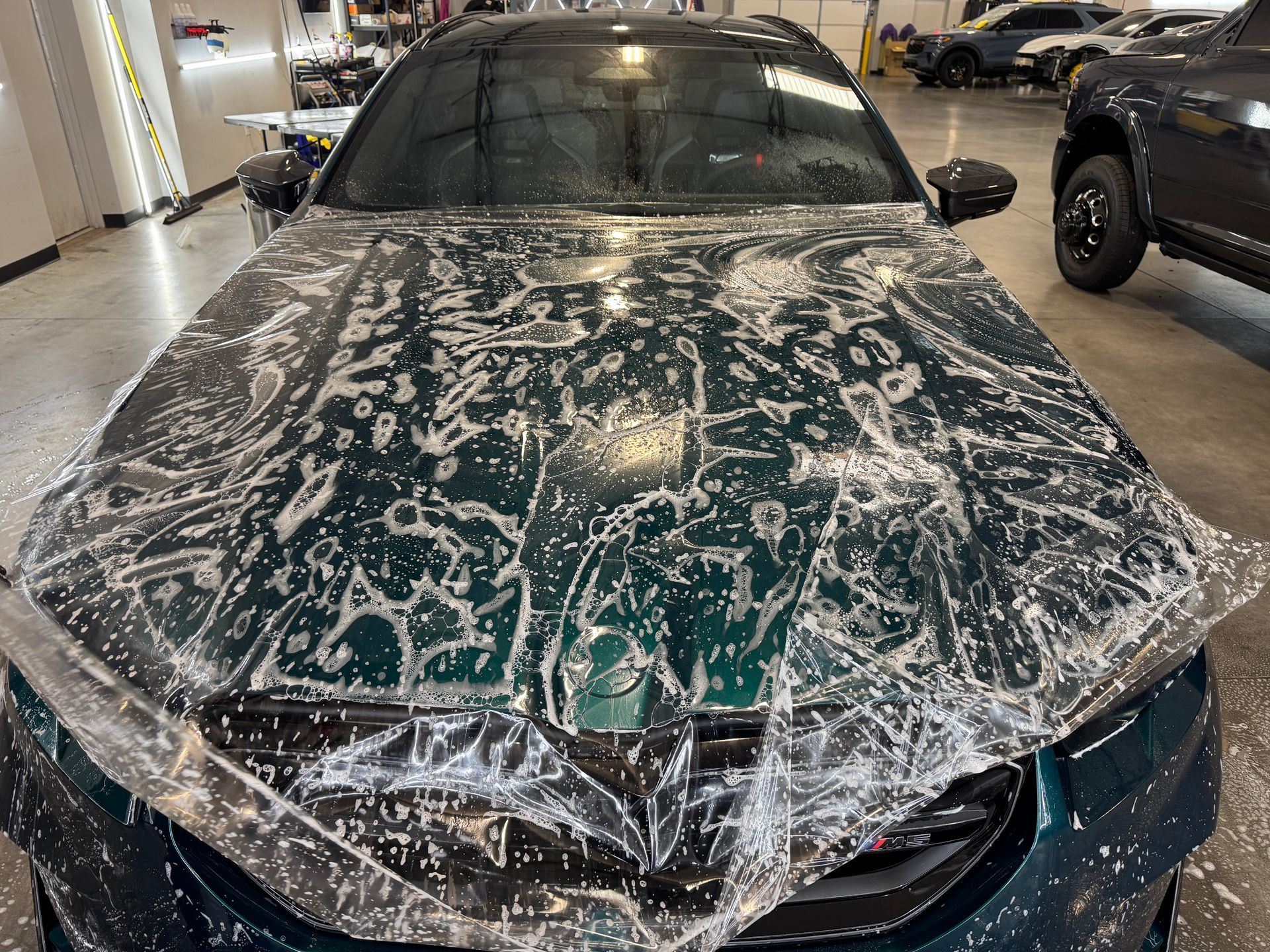 Green car in a garage, covered with thick white soap foam during a wash.