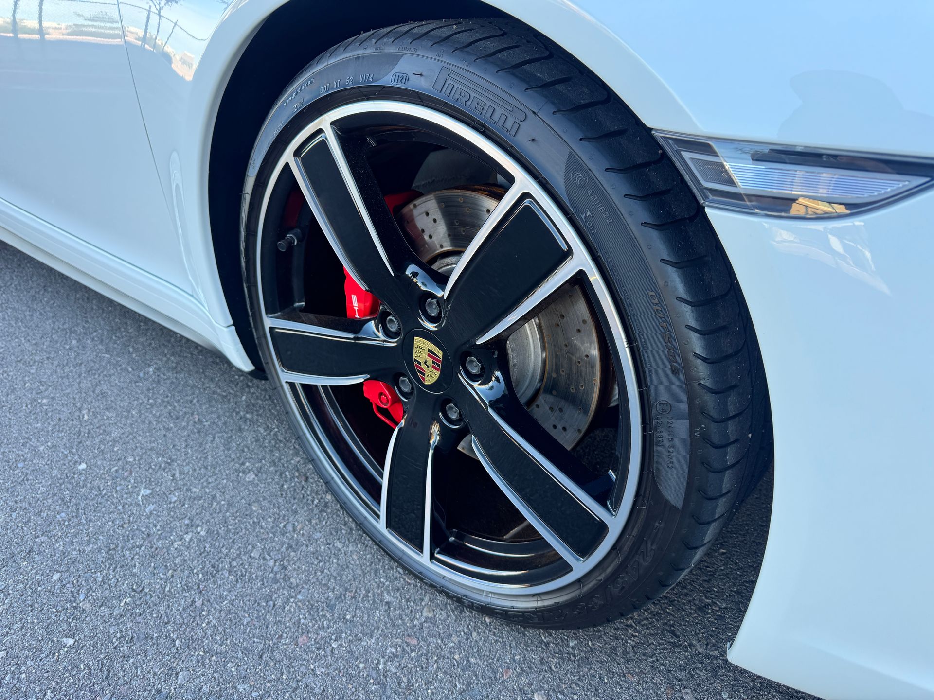 Close-up of a white sports car’s front wheel with black alloy rim and red brake caliper.