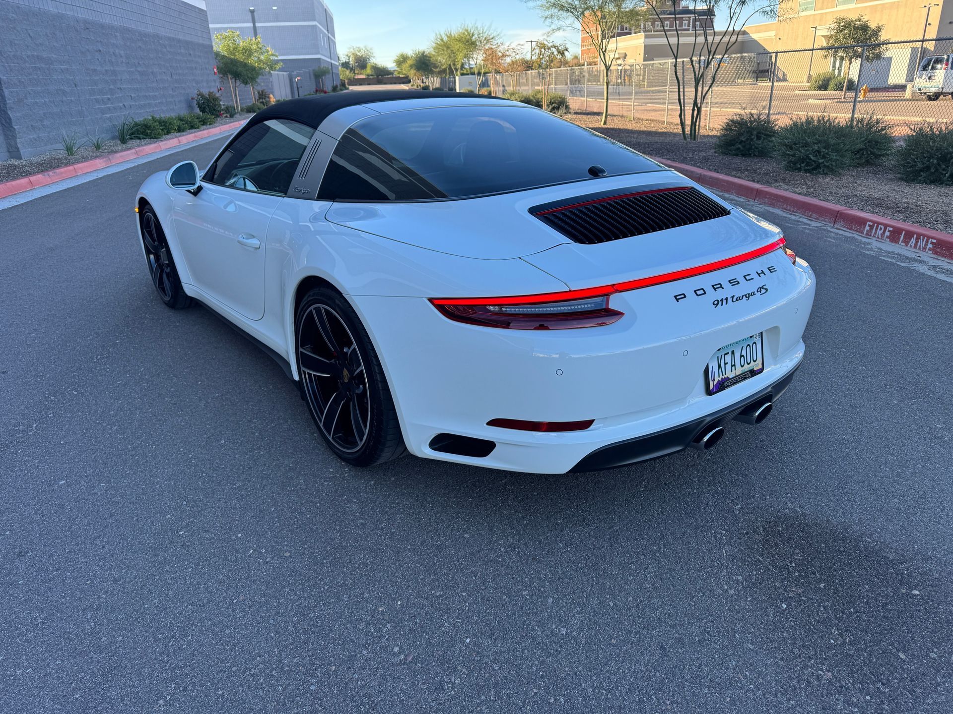 White Porsche 911 on a street, rear three-quarter view, with black roof and wheels
