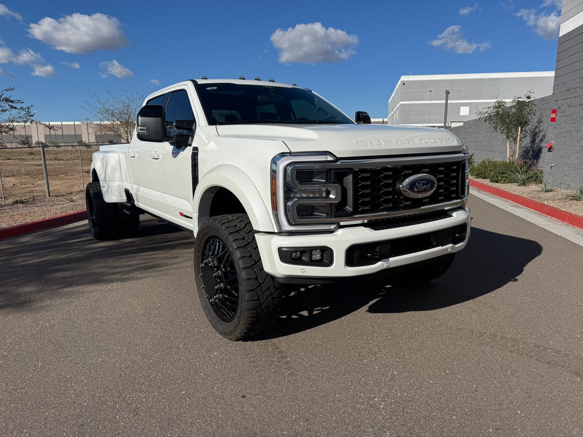 White lifted Ford pickup truck parked outdoors on a sunny street, front three-quarter view