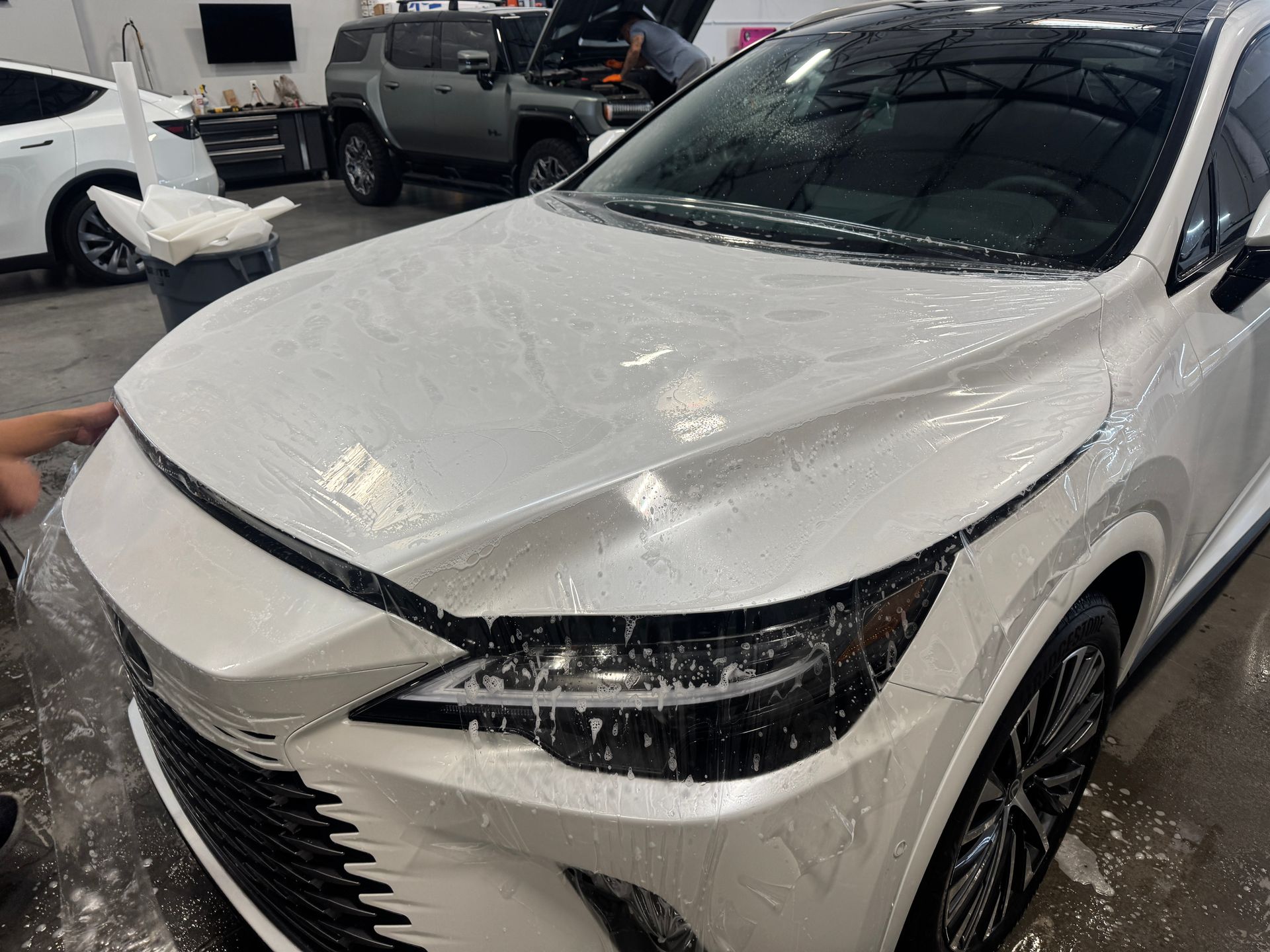 White SUV with a dented hood, covered in foam, in a car wash bay
