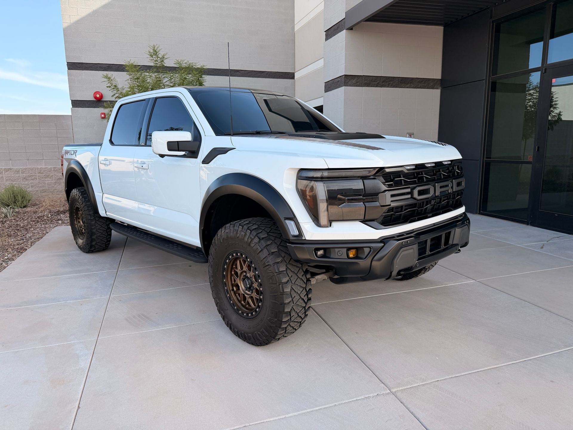A white lifted Ford pickup truck parked by a modern building.