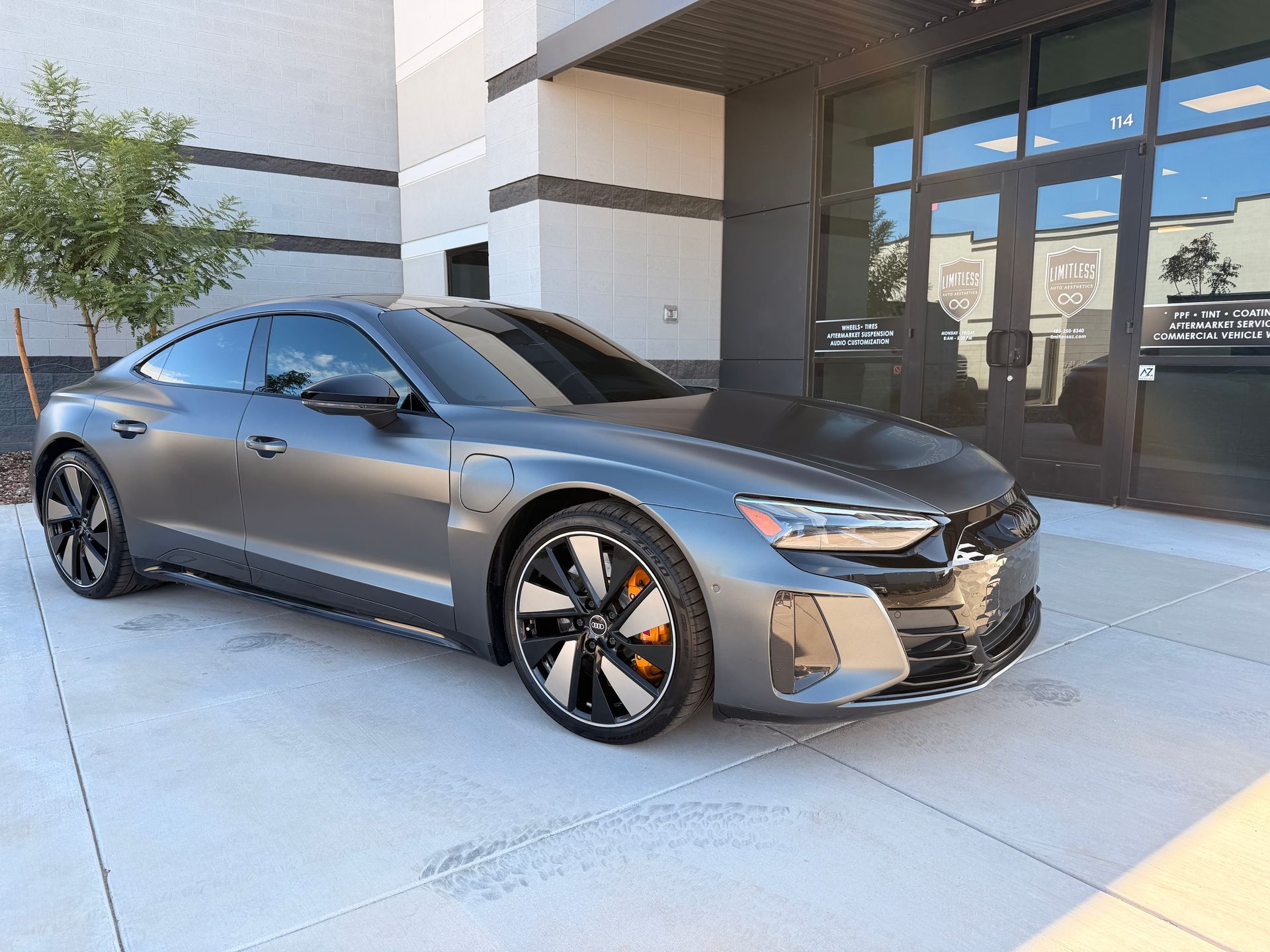 Gray sports coupe parked outside a modern building with glass doors and a concrete walkway
